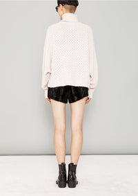 back view of woman standing by a wall wearing SWEATER TURTLENECK - KNIT PEARL beige